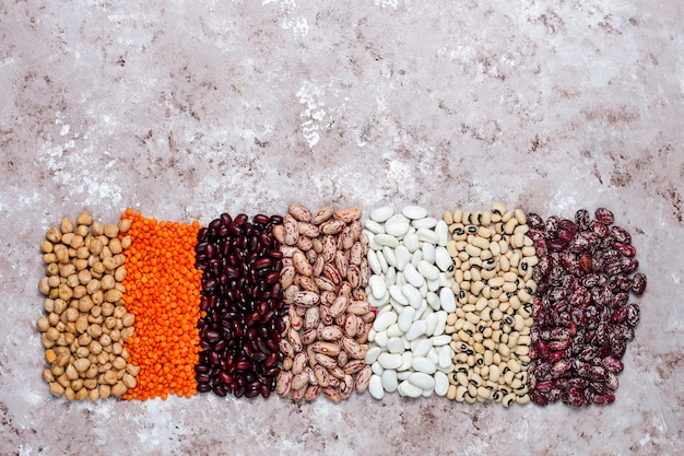 Surtido de legumbres y frijoles en diferentes tazones sobre fondo de piedra clara. Vista superior. Comida sana de proteínas veganas.