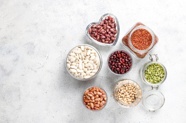 Surtido de legumbres y frijoles en diferentes tazones sobre fondo de piedra clara. Vista superior. Comida vegana saludable de proteínas.