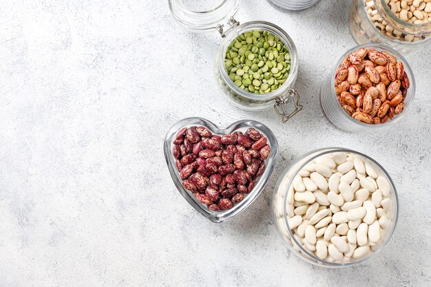 Surtido de legumbres y frijoles en diferentes tazones sobre fondo de piedra clara. Vista superior. Comida vegana saludable de proteínas.