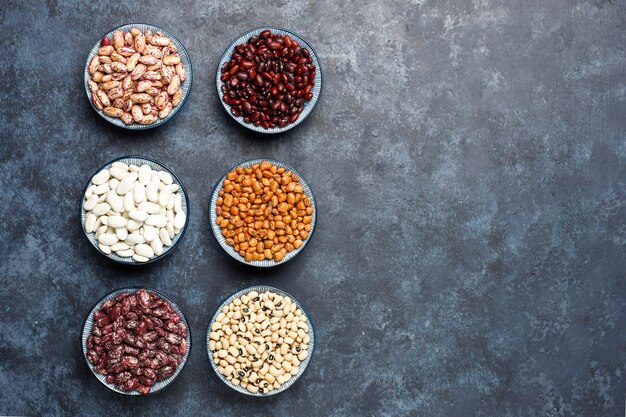 Surtido de legumbres y frijoles en diferentes tazones sobre superficie de piedra clara. Vista superior. Comida sana de proteínas veganas.