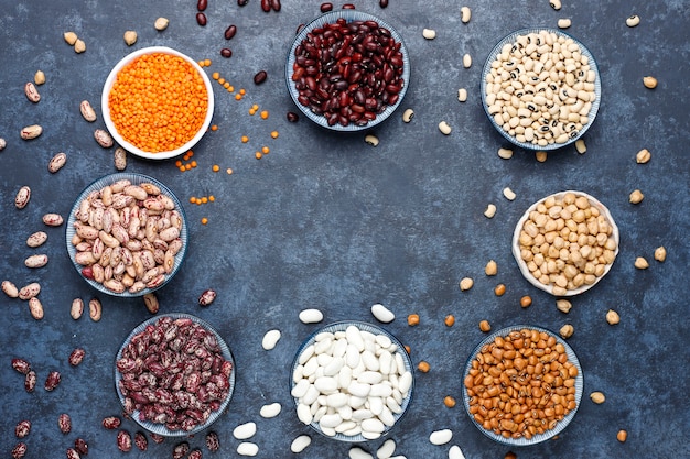 Foto gratuita surtido de legumbres y frijoles en diferentes tazones sobre superficie de piedra clara. vista superior. comida sana de proteínas veganas.