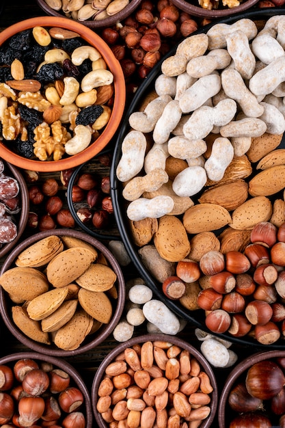 Surtido de nueces y frutas secas en diferentes cuencos y platos con nuez, pistachos, almendras, maní, anacardo, piñones, vista superior