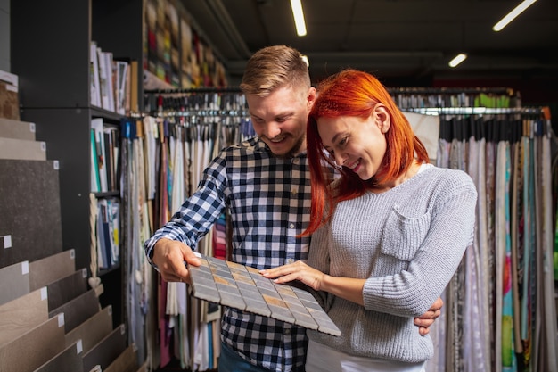 Surtido. Pareja eligiendo textiles en la tienda de decoración del hogar, tienda. Realización de diseño de interiores de viviendas durante la cuarentena. El hombre y la mujer felices, la familia joven se ven soñadores, alegres eligiendo materiales.