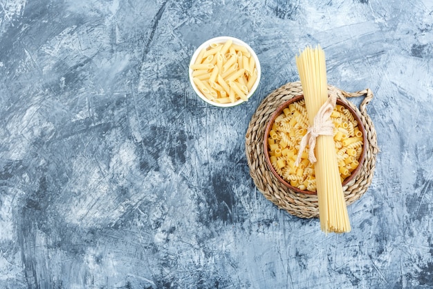 Surtido de pastas en tazones de fuente sobre yeso gris y fondo de mantel de mimbre. vista superior.