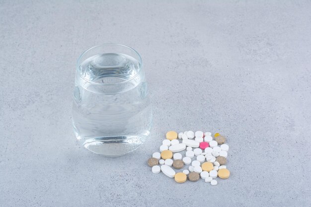 Surtido de píldoras de medicina farmacéutica y vaso de agua.