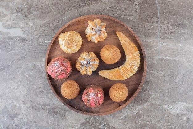 Surtido de postres con galletas, bollos y cupcakes en una bandeja sobre la superficie de mármol