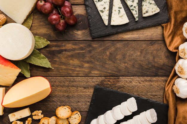 Surtido de quesos; uvas; rebanada de pan nogal en mesa de madera oscura