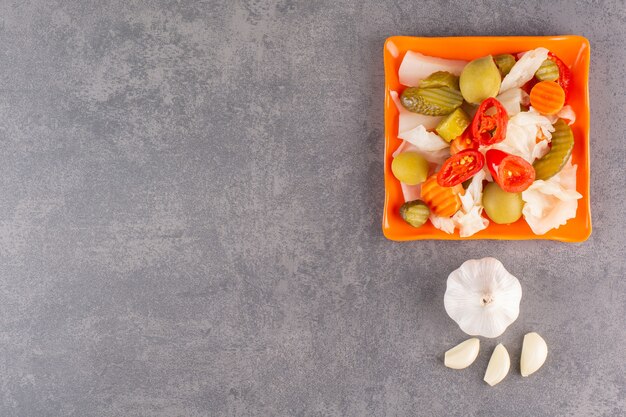 Surtido de verduras encurtidos en un recipiente colocado sobre la mesa de piedra.