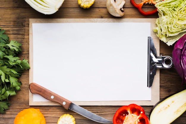 Surtido de verduras sobre fondo de madera con portapapeles vacío