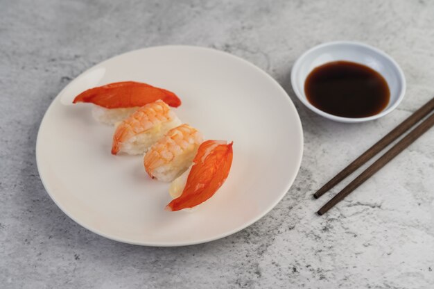 El sushi está en un plato con palillos y salsa en un piso de cemento blanco.