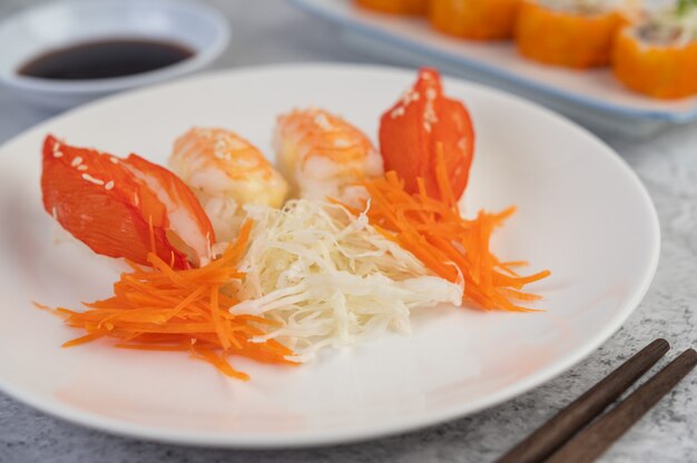 El sushi está en un plato con palillos y salsa en un piso de cemento blanco.