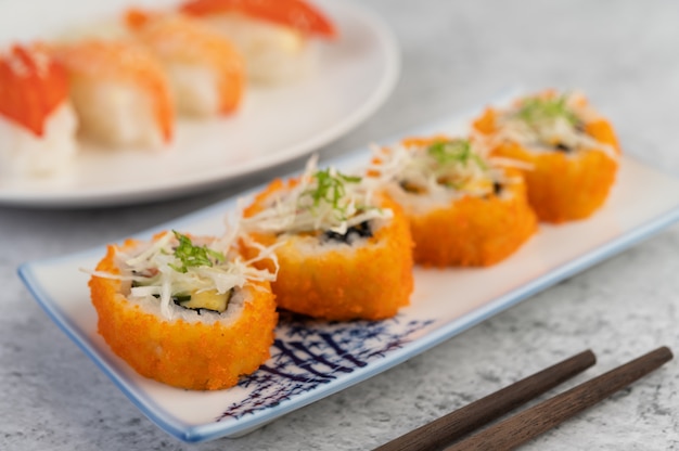 El sushi está en un plato con palillos y salsa en un piso de cemento blanco.