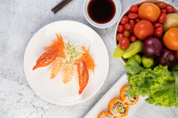 El sushi está en un plato con palillos y salsa en un piso de cemento blanco.