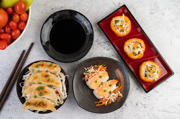 El sushi está en un plato con palillos y salsa en un piso de cemento blanco.