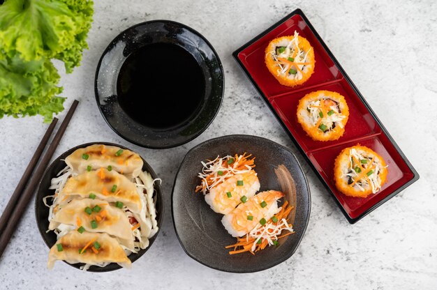 El sushi está en un plato con palillos y salsa en un piso de cemento blanco.