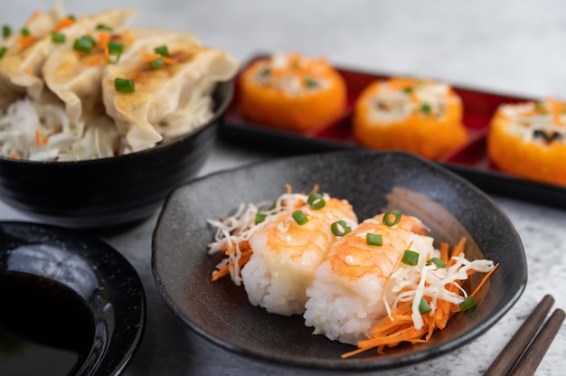 El sushi está en un plato con palillos y salsa en un piso de cemento blanco.