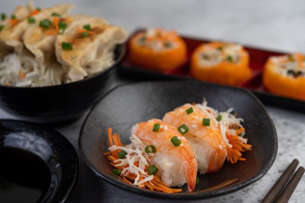 El sushi está en un plato con palillos y salsa en un piso de cemento blanco.