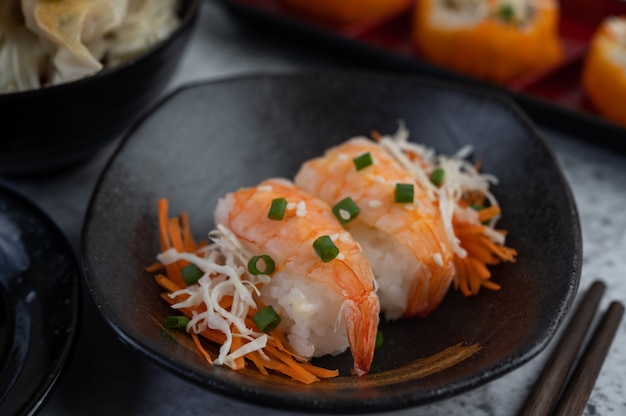 El sushi está en un plato con palillos y salsa en un piso de cemento blanco.