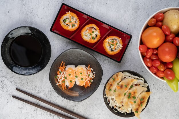 El sushi está en un plato con palillos y salsa en un piso de cemento blanco.