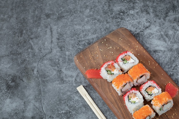 Sushi maki con caviar rojo y queso crema sobre una tabla de madera.