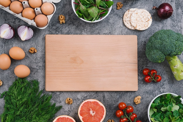 Foto gratuita tabla de cortar de madera en blanco con verduras crudas y pastel de arroz inflado sobre fondo de hormigón