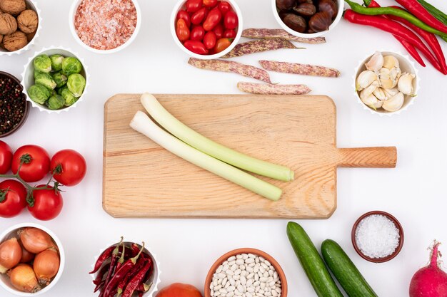 Tabla de cortar de madera con espacio de copia vacío rodeado de diferentes verduras en un tazón redondo sobre mesa blanca