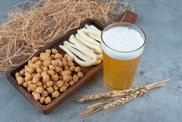 Una tabla de cortar de madera de guisantes y queso con un vaso de cerveza. Foto de alta calidad