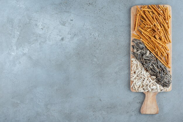 Una tabla de cortar de madera llena de semillas de girasol y palitos de pan. Foto de alta calidad