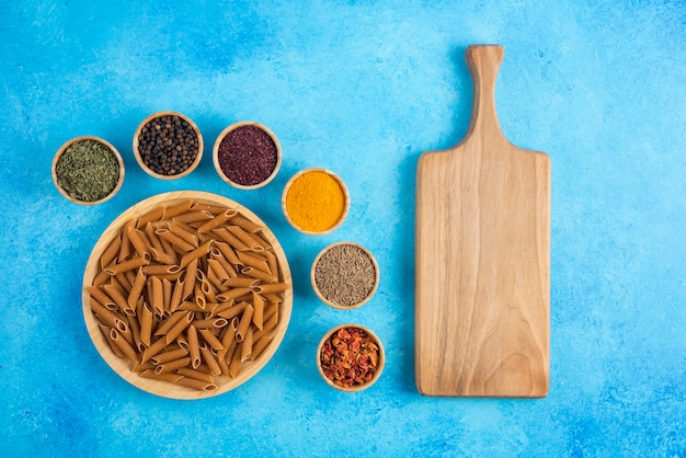 Foto gratuita tabla de cortar de madera y pasta cruda marrón con especias sobre fondo azul.