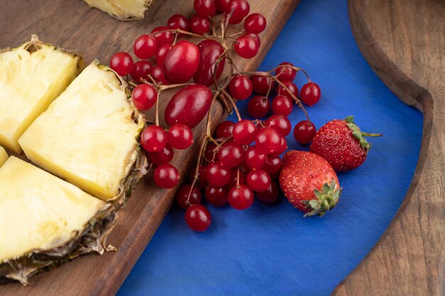 Una tabla de cortar de madera con rodajas de piña y grosella