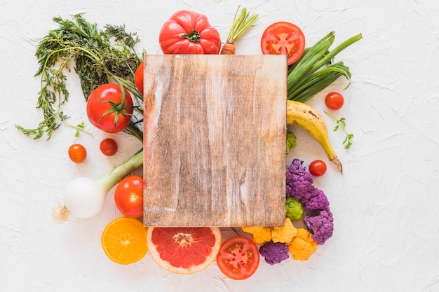 Foto gratuita tabla de cortar de madera sobre las verduras y frutas en el telón de fondo de textura blanca