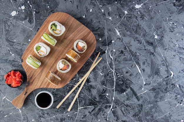 Tabla de cortar de madera de varios rollos de sushi sobre mesa de mármol.