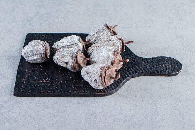 Tabla de cortar negra de frutos secos de caqui sobre fondo de piedra.