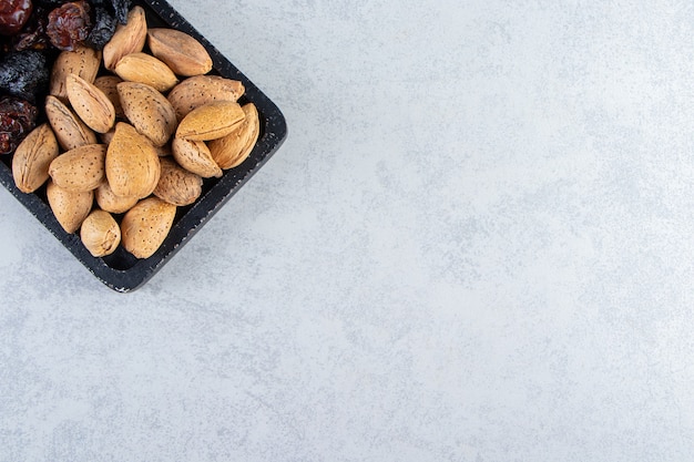 Tabla de cortar negra llena de dátiles secos y nueces sobre fondo de piedra.