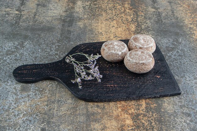 Una tabla de cortar oscura con pan de jengibre y flores marchitas.