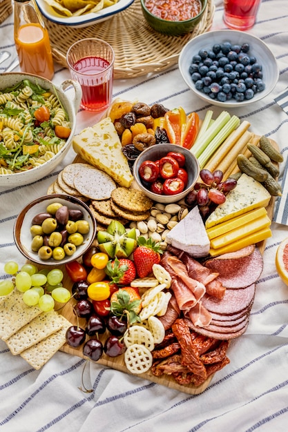 Foto gratuita tabla de embutidos con embutidos, frutas frescas y queso sobre un paño de picnic