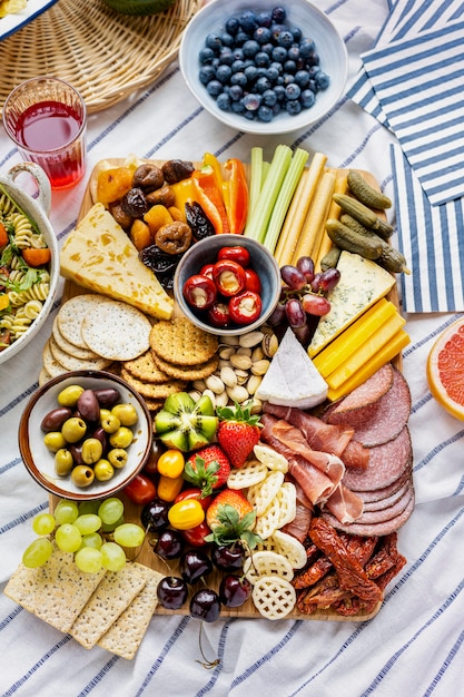 Foto gratuita tabla de embutidos con embutidos, frutas frescas y queso sobre un paño de picnic