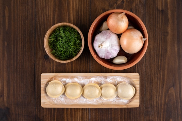 Foto gratuita una tabla de madera de albóndigas pelmeni caseras con un cuenco de barro de cebollas.