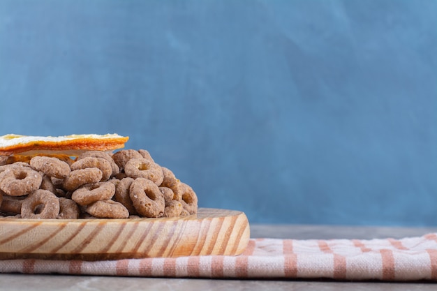 Una tabla de madera de anillos de cereal de chocolate saludables con una rodaja de fruta naranja.