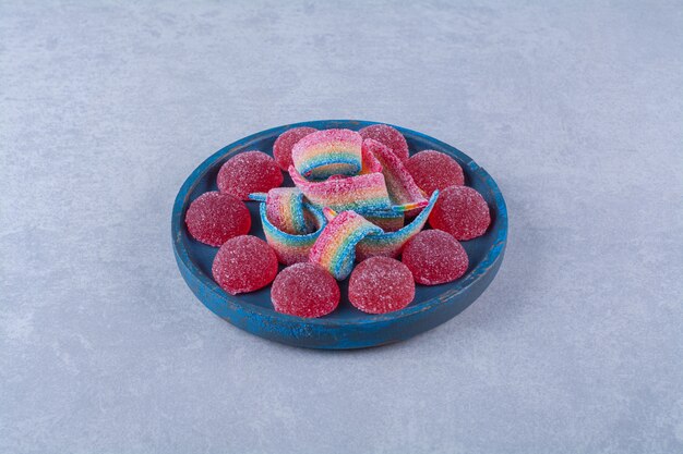 Una tabla de madera azul de caramelos de gelatina roja azucarada con regaliz dulce de arco iris. Foto de alta calidad