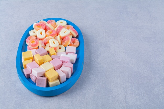 Una tabla de madera azul de caramelos de gelatina roja azucarada con regaliz dulce de arco iris.