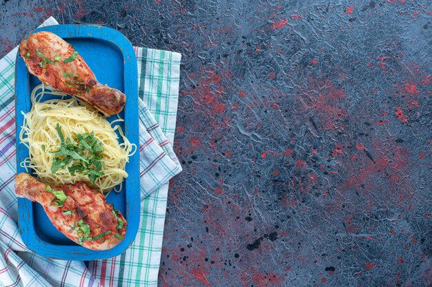 Una tabla de madera azul de carne de muslos de pollo al horno con espagueti.