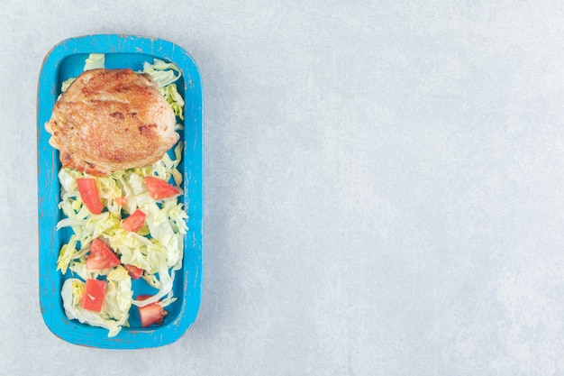 Una tabla de madera azul de carne de pollo con ensalada de verduras.