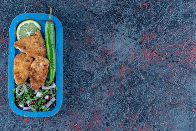 Una tabla de madera azul de chuleta de pollo al horno con ensalada de verduras.