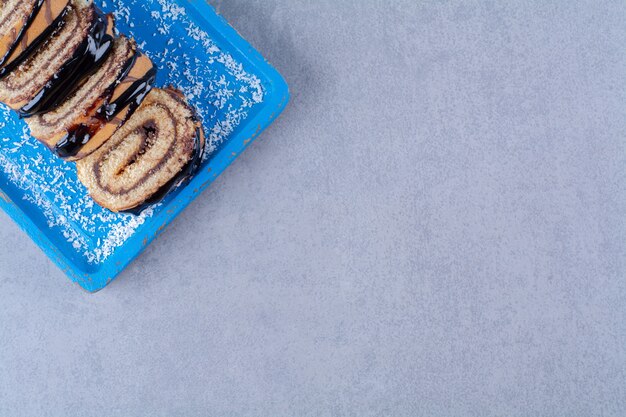 Una tabla de madera azul de rollo dulce en rodajas con jarabe de chocolate.