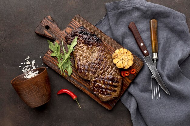 Tabla de madera con carne a la parrilla y cubiertos.