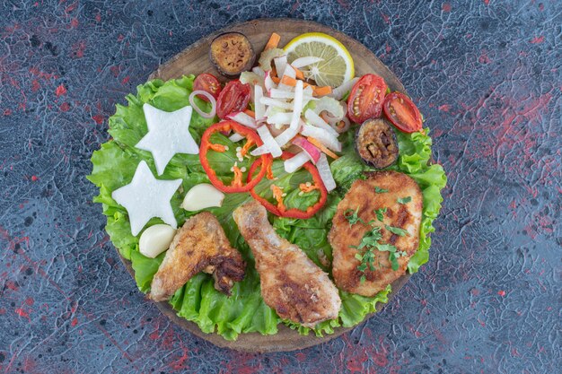 Una tabla de madera con carne de pollo al horno y verduras.