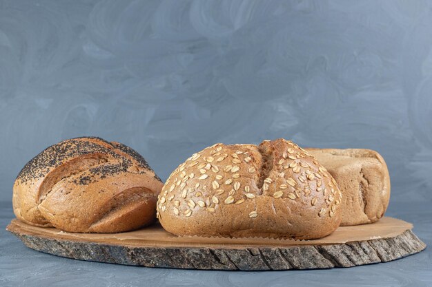 Tabla de madera debajo de tres hogazas de pan sobre mesa de mármol.