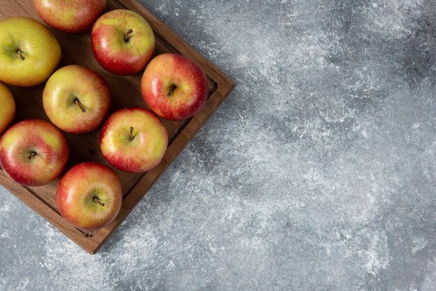 Tabla de madera de deliciosas manzanas frescas sobre superficie de mármol.