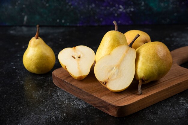 Tabla de madera de deliciosas peras amarillas sobre superficie negra.